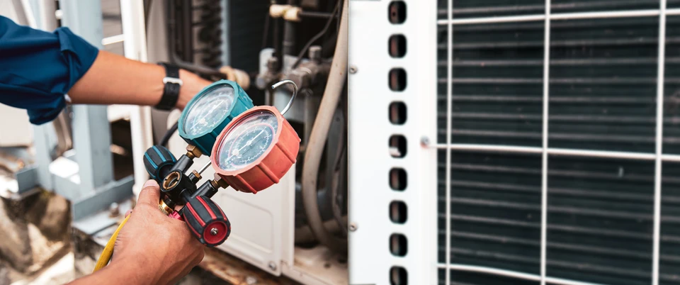 Technicien en climatisation travaillant sur unité extérieure avec manomètres de réfrigération