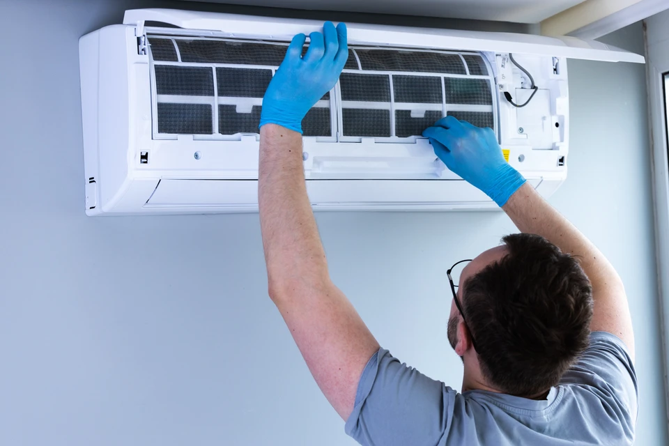 Technicien en combinaison blanche effectuant la maintenance d'une unité extérieure de climatisation sur terrasse ensoleillée
