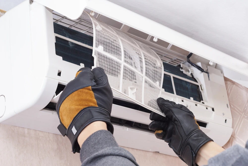 Un technicien en uniforme bleu nettoie une unité de climatisation murale split avec un chiffon bleu