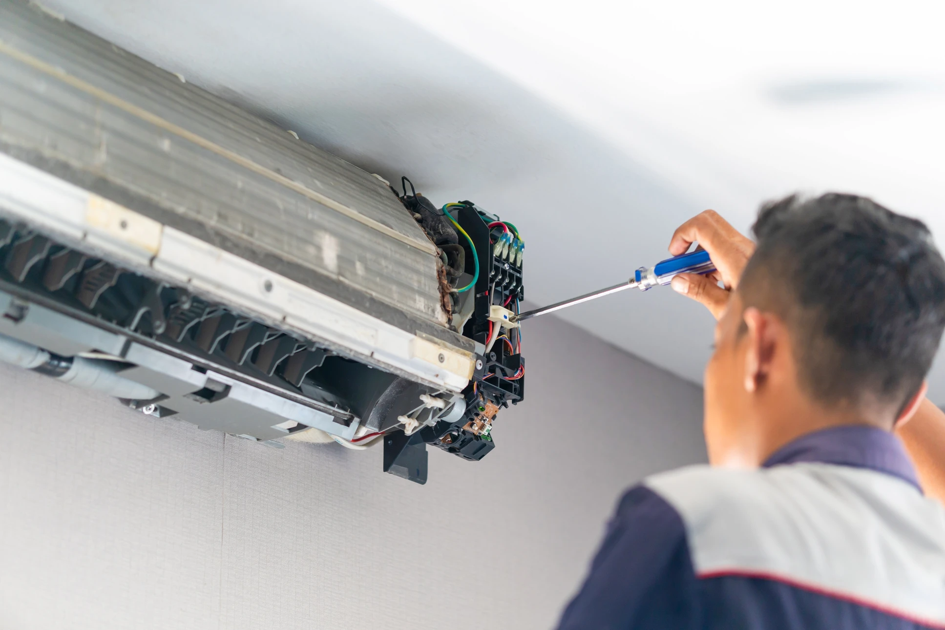 Technicien tenant un manifold de climatisation avec deux manomètres à cadrans colorés bleu et rouge dans un environnement intérieur professionnel