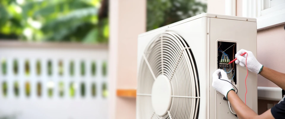 Technicien en combinaison blanche effectuant la maintenance d'une unit&eacute; ext&eacute;rieure de climatisation sur terrasse ensoleill&eacute;e
