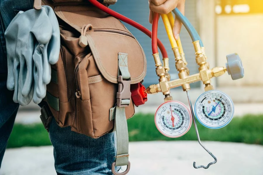 Technicien tenant un manifold de climatisation avec deux manomètres à cadrans colorés bleu et rouge dans un environnement intérieur professionnel